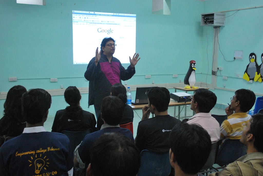 Presenter speaking to students in a classroom with a projected Google page